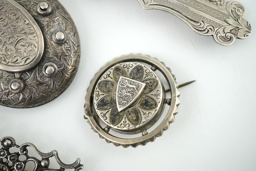 An oval engraved white metal enclosed locket and chain and five assorted white metal brooches. Condition - fair